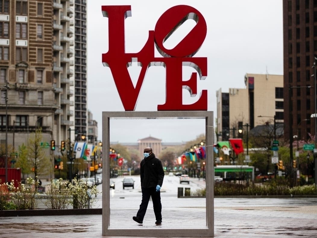 A person wears a protective face mask and gloves as a precaution against the coronavirus while walking by the Robert Indiana sculpture "LOVE" at John F. Kennedy Plaza in Philadelphia.