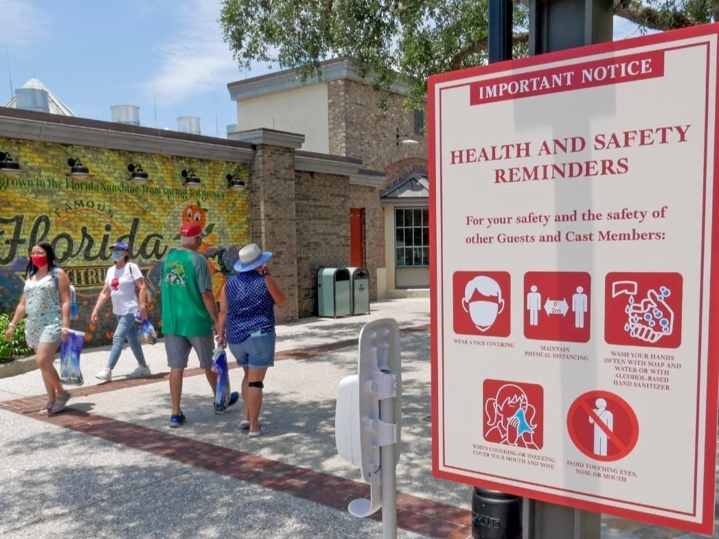 Signs remind patrons to wear masks and follow other coronavirus pandemic protocols as they stroll through the Disney Springs shopping, dining and entertainment complex in Lake Buena Vista, Florida.