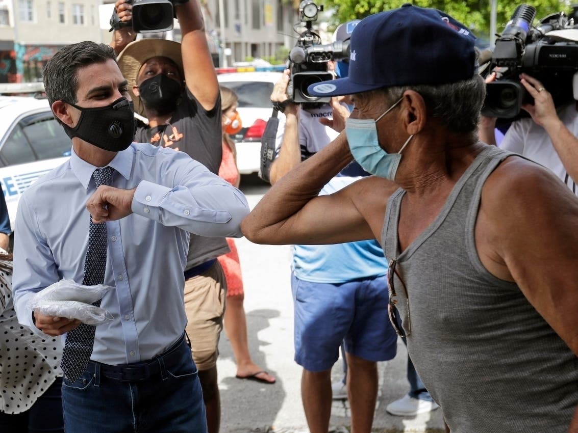 Benigno Enriquez (right) elbow-bumps Miami Mayor Francis Suarez as Suarez hands out masks to help prevent the spread of the new coronavirus.