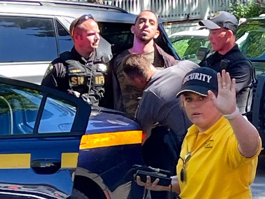 Law enforcement officers detain a person outside the Chautauqua Institution on Friday after renowned author Salman Rushdie was attacked and stabbed while preparing to speak at an institution literary event.