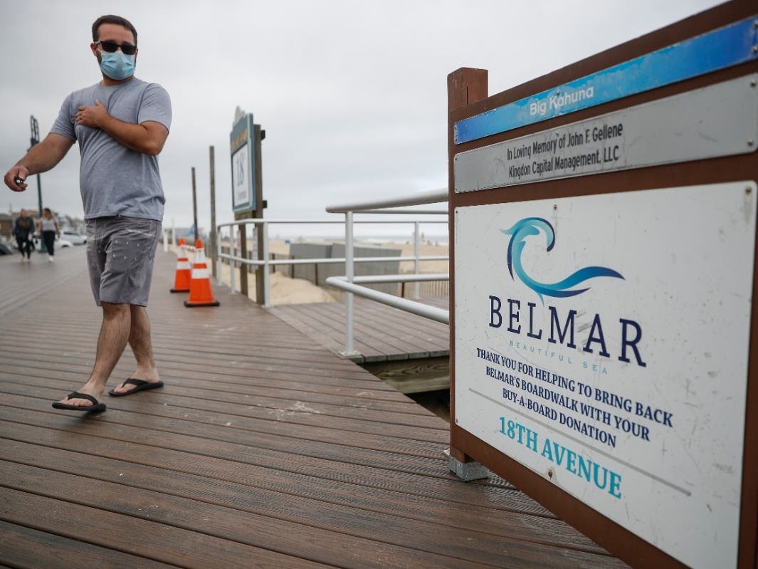 A pedestrian wearing a protective mask walks along the boardwalk and a mostly empty beach, Saturday, May 23, 2020, in Belmar, N.J.