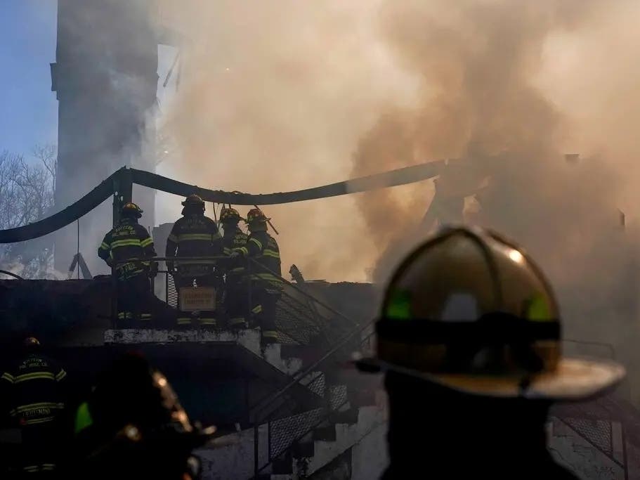 This photo from March 23, 2021, shows firefighters at the smoldering aftermath of a fire that burned down the Evergreen Court Home for Adults in Spring Valley, NY. Six people face charges in connection with the fire that killed a firefighter and resident.