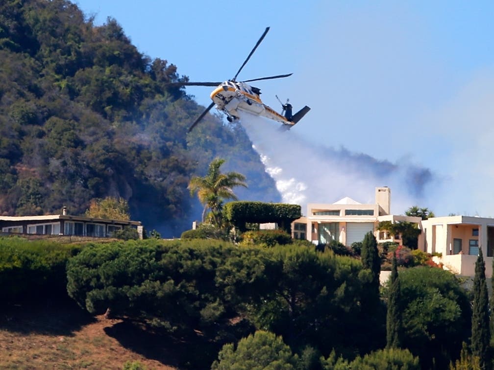 A Los Angeles County Fire Department helicopter makes a water drop as flames from a wildfire threaten homes on a ridgeline in the Pacific Palisades area of Los Angeles Monday, Oct. 21, 2019