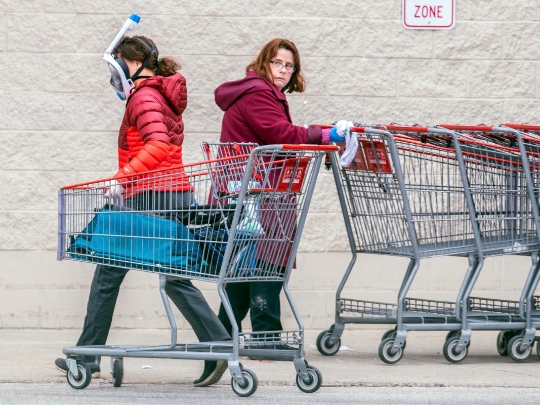A Costco employee, right, looks towards a shopper wearing a mask and snorkel to go shopping, as she sanitizes carts that are returned from the parking lot to help reduce the spread of coronavirus.