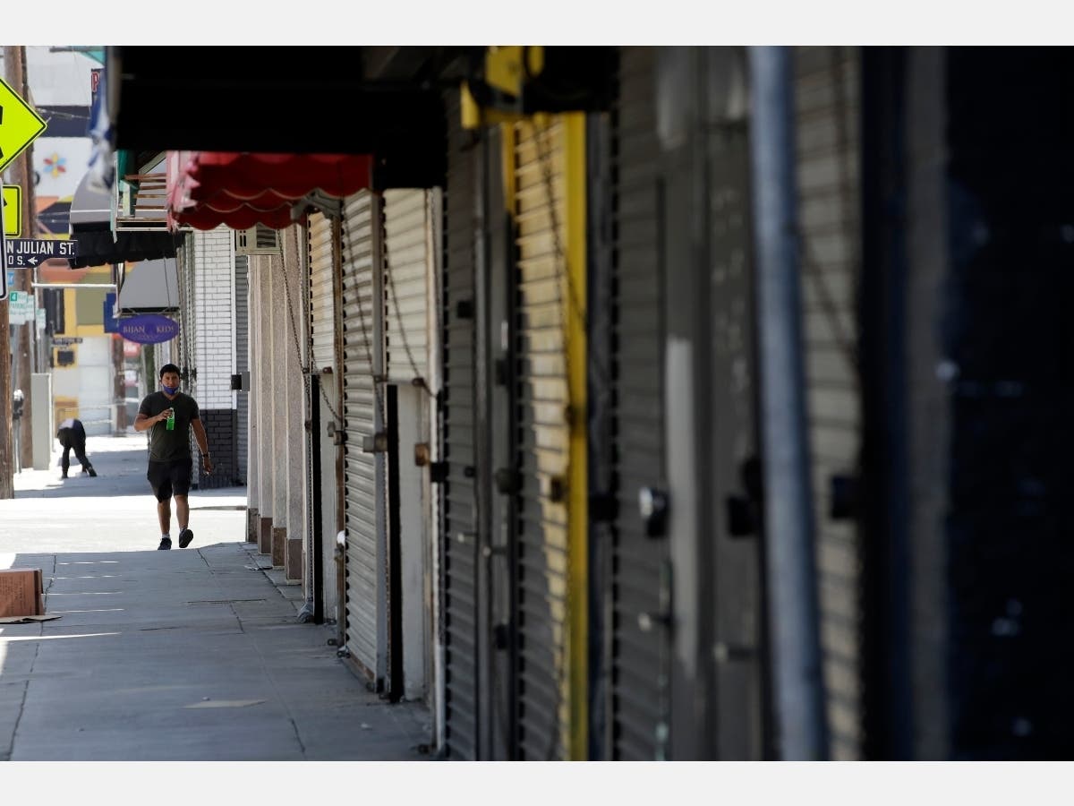 A man walk past closed-off stores Monday, May 4, 2020, in the fashion district of Los Angeles. Amid more defiance from local governments, California Gov. Gavin Newsom said Monday that some businesses can reopen as early as Friday with restrictions.