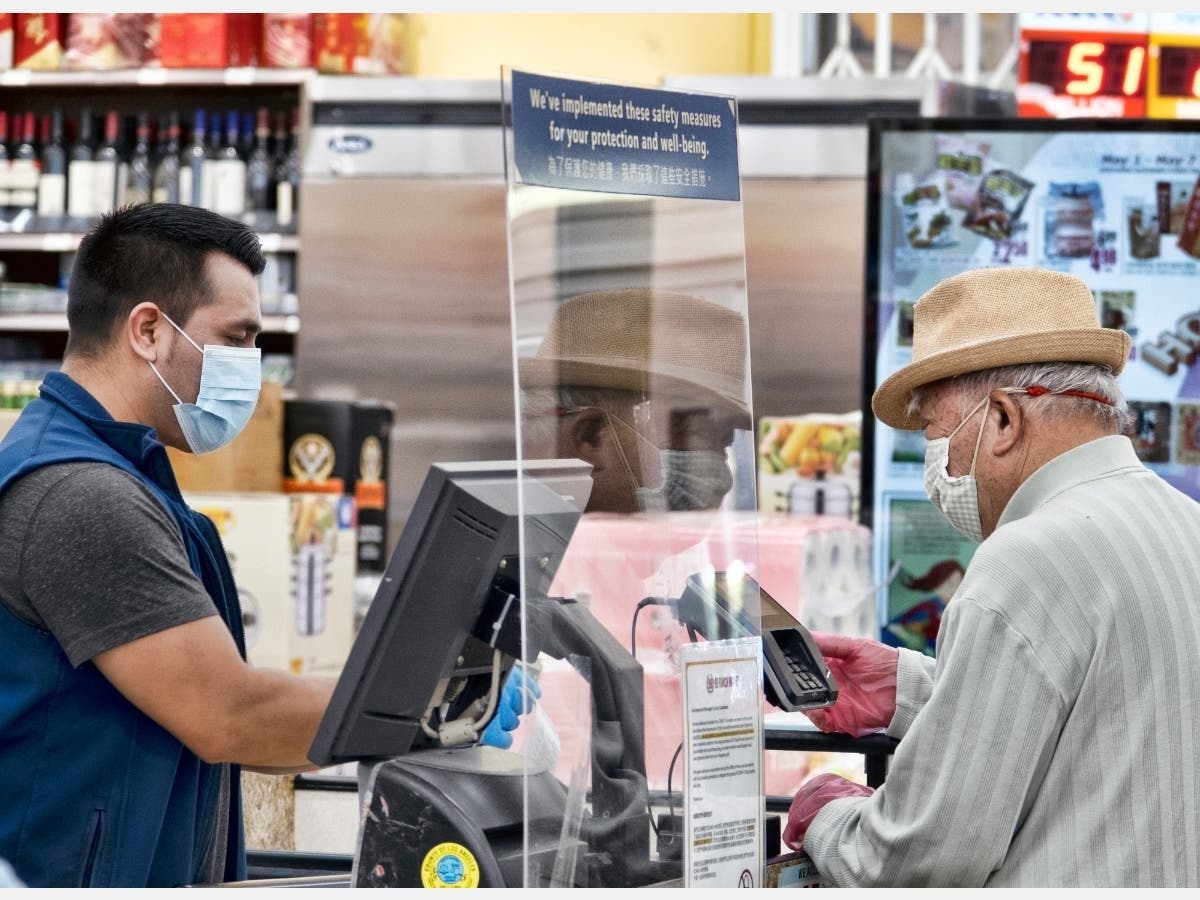 A grocery worker, wearing a protective mask and gloves, helps checking out a customer from behind a plexiglass barrier at the 99 Ranch Market in the Van Nuys section of Los Angeles on Tuesday May, 5, 2020. 