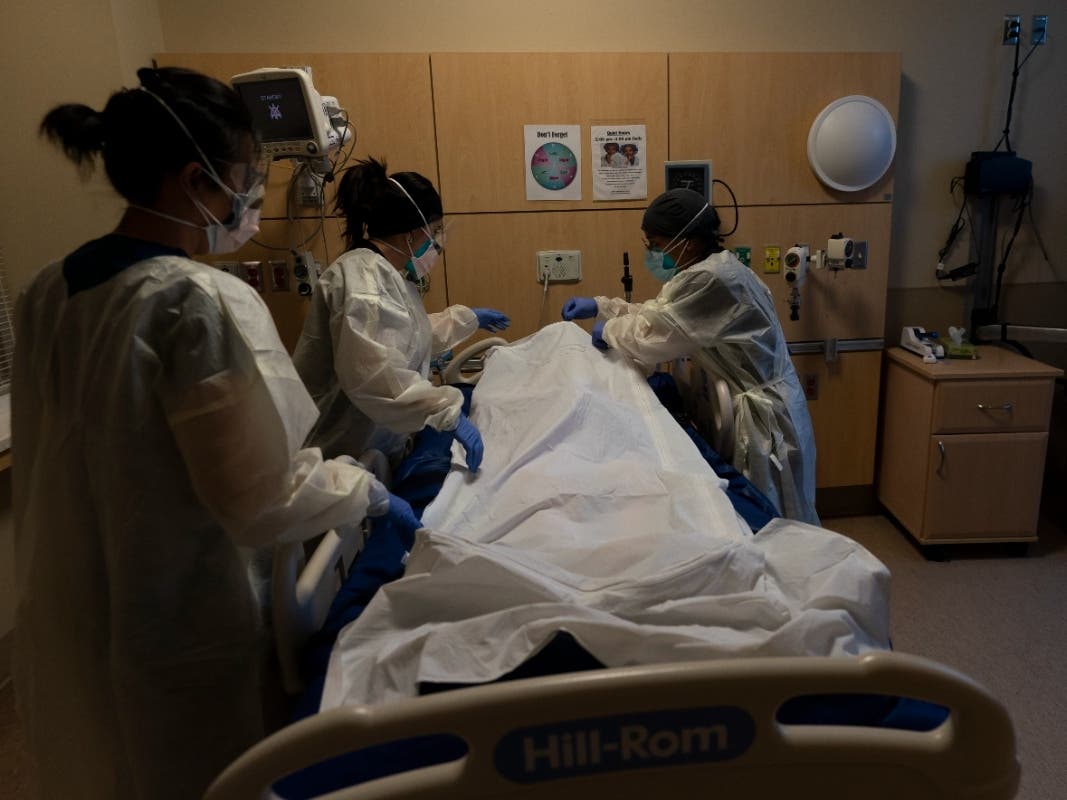 Registered nurse Bryan Hofilena, from right, certified nursing assistant Alexis Figueroa and registered nurse Emily Yu zip up a body bag holding a COVID-19 victim after giving postmortem care at Providence Holy Cross Medical Center in Los Angeles Dec. 14.