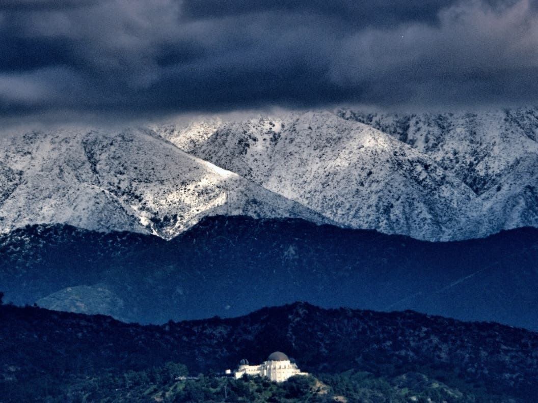 Storm clouds and snow are seen over the San Gabriel mountain range behind Griffith Observatory in the Hollywood Hills. 