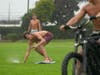 Surfers Caspian Ryan, middle, skims on grass as Adrian Zimmernan pulls him with a rope attached to an electric bike pulling the board on a fully soaked lawn under heavy rain at Cannon Park in Carlsbad, Calif., Sunday.