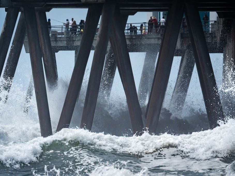 People walk on a pier as large waves from Hurricane Marie break on the shore, Monday, Sept. 7, 2026, on Huntington Beach, southern Calif.