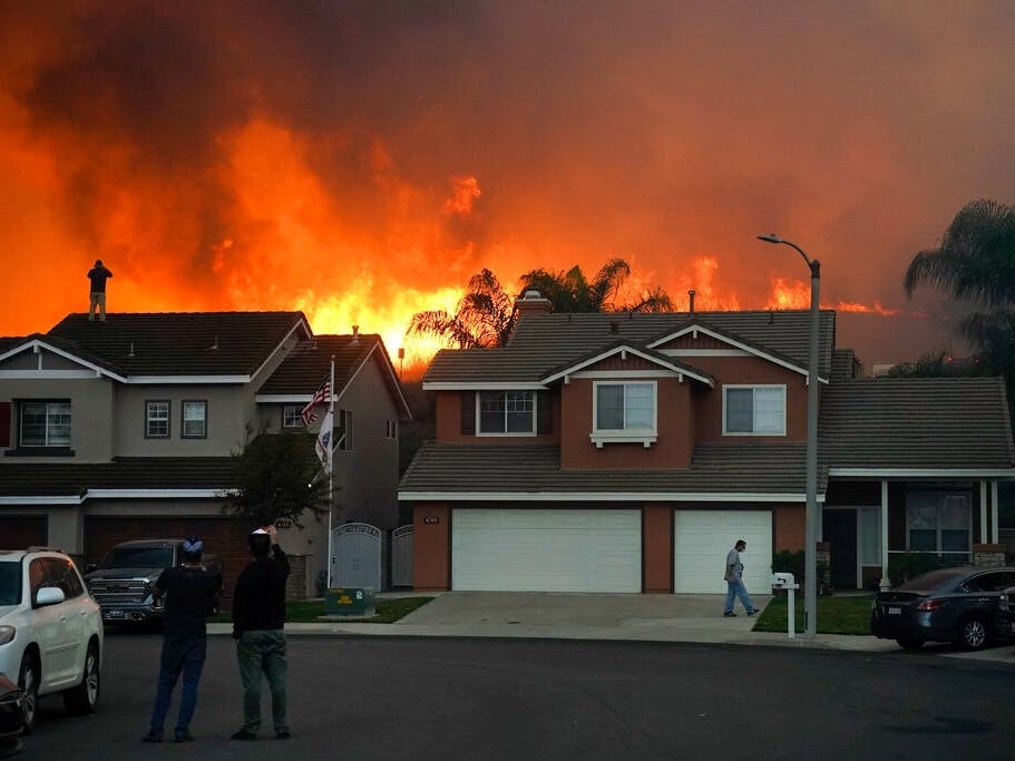 In this Oct. 27, 2020 photo, residents watch as the Blue Ridge Fire burns above blacked-out homes in Chino Hills, Calif. Southern California amid Santa Ana winds. By Friday, wind gusts could reach 70 mph in the mountains, according to the weather service