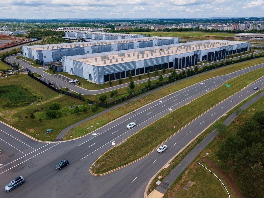 Cars drive past data centers in Ashburn, Virginia, one of the main hubs of northern Virginia’s huge data-center concentration. The region is the world’s largest data center market, with about 4,500 megawatts of capacity as of mid-2026, according to CBRE.