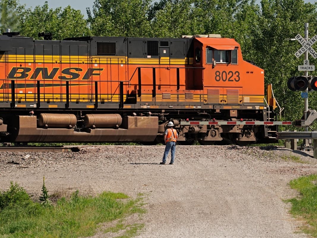 A worker watches as a freight train moves through a crossing Tuesday, a mile west of the crossing near Mendon, where an Amtrak train derailed after striking a dump truck Monday.