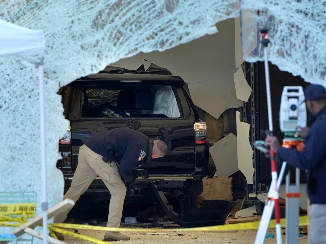 A law enforcement official, center, examines an SUV inside an Apple store, Monday, Nov. 21, 2022, in Hingham, Mass. The crash left a large hole in the glass front of the Apple store.