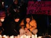 Women place candles at a memorial while a man holds a sign during a vigil outside Monterey Park City Hall, blocks from the Star Ballroom Dance Studio on Tuesday, Jan. 24, 2023, in Monterey Park, Calif.