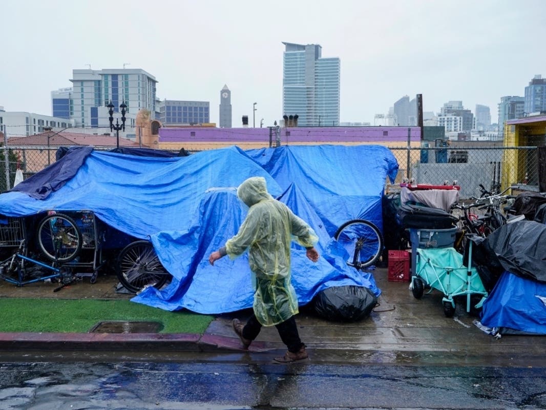 Homeless people use plastic tarps to shield themselves from a light rain brought by Tropical Storm Hilary in downtown San Diego, Sunday, Aug. 20, 2023.