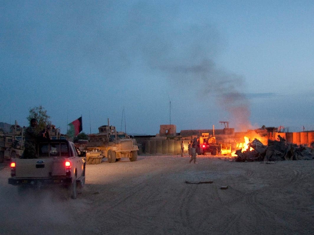 In this April 28, 2011, photo, an Afghan National Army pickup truck passes parked U.S. armored military vehicles, as smoke rises from a fire in a trash burn pit at Forward Operating Base Caferetta Nawzad, Helmand province south of Kabul, Afghanistan. 