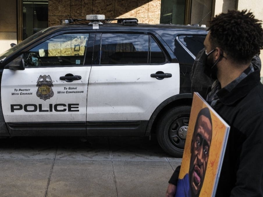 A man carrying a portrait of George Floyd looks on at a police cruiser as demonstrators march in honor of George Floyd on March 7, 2021 in Minneapolis, Minnesota.