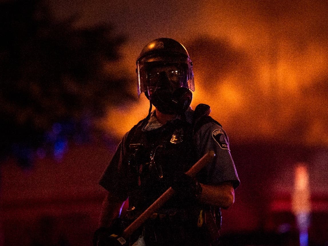 A police officer stands with a baton as a fire burns inside of an Auto Zone store near the Third Police Precinct on May 27, 2020, in Minneapolis, Minnesota.