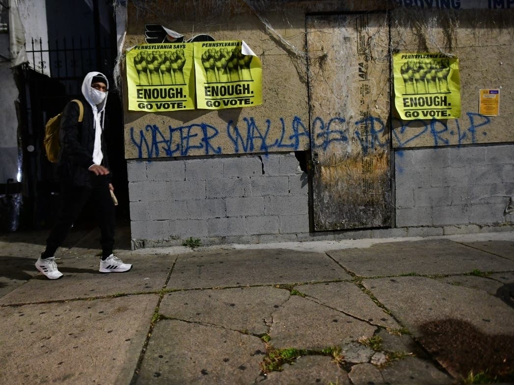 A man walks past posters reading "ENOUGH GO VOTE" and a "WALTER WALLACE RIP" graffiti during a citywide curfew on October 28, 2020 in Philadelphia, Pennsylvania