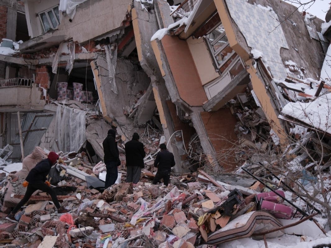 Local people look at a collapsed building on Monday in Elbistan, Turkey, following a deadly earthquake.