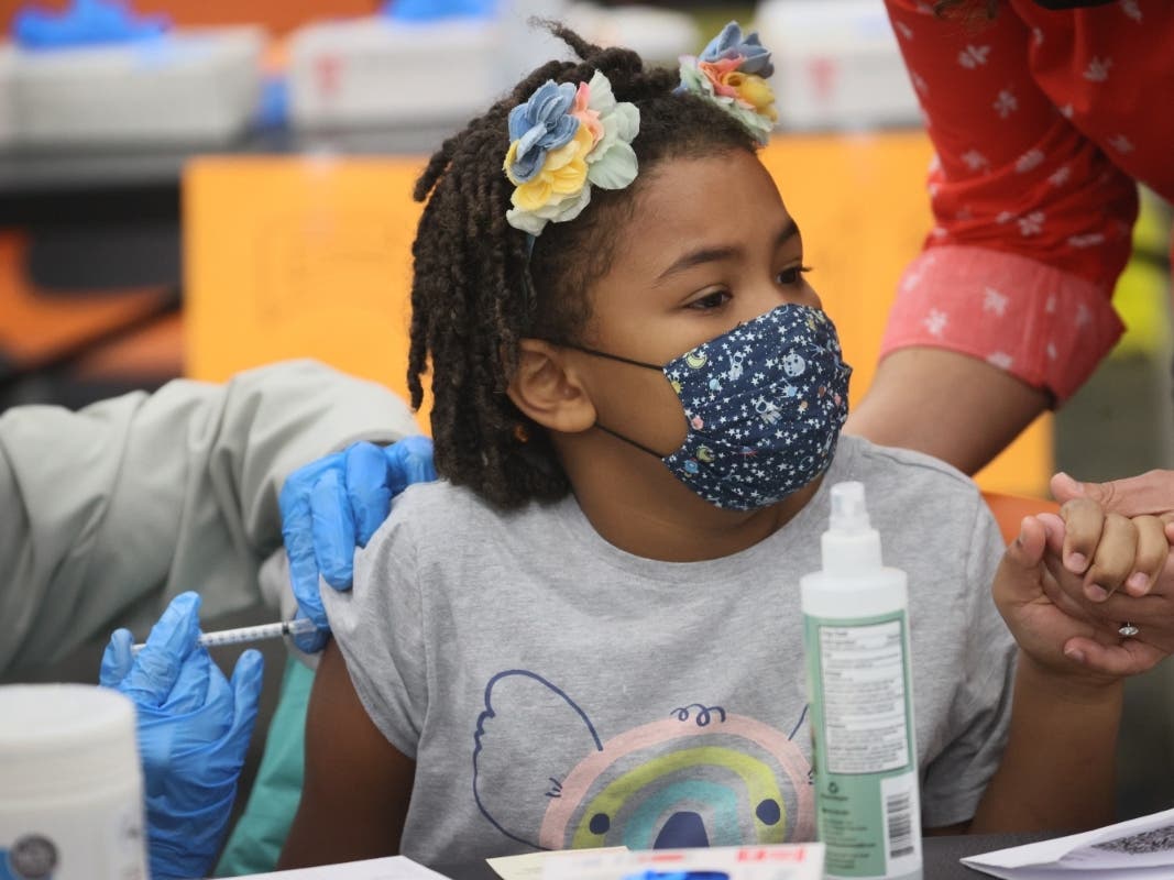 File photo: A third-grade student holds her mother's hand while getting a COVID-19 vaccine.