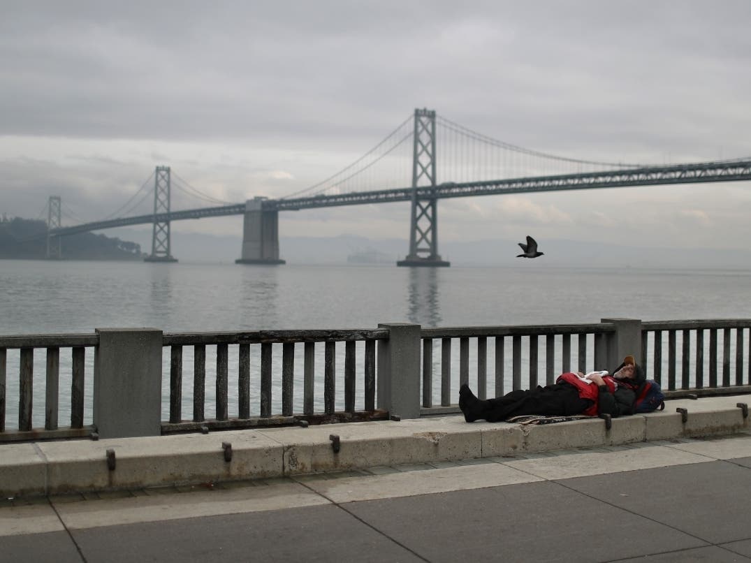 A homeless man sleeps on the sidewalk near the San Francisco–Oakland Bay Bridge on December 05, 2019 in San Francisco, California