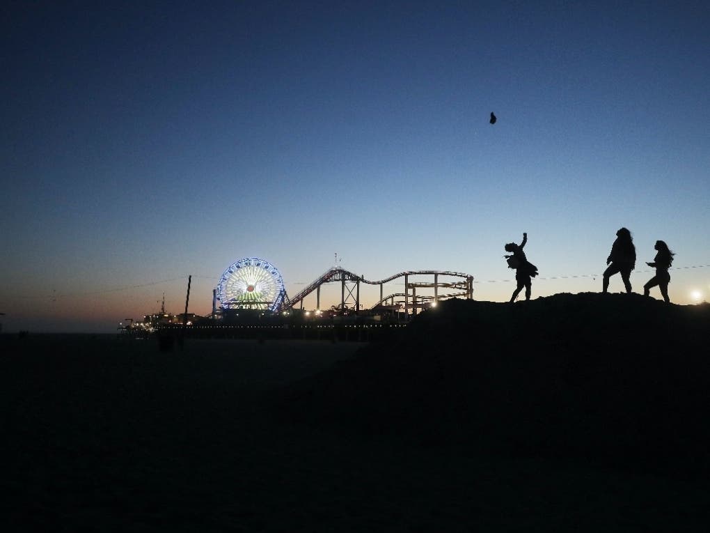 A man tosses his hate into the air at dusk at the beach, with the shuttered Santa Monica Pier in the background, on the day Los Angeles County reopened its beaches which had been closed due the coronavirus pandemic, on May 13, 2020 in Santa Monica, Calif.