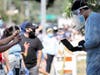 A testing associate dressed in personal protective equipment (PPE) helps people waiting in line to check in at a COVID-19 testing center at Lincoln Park amid the coronavirus pandemic on July 07, 2020 in Los Angeles, California.
