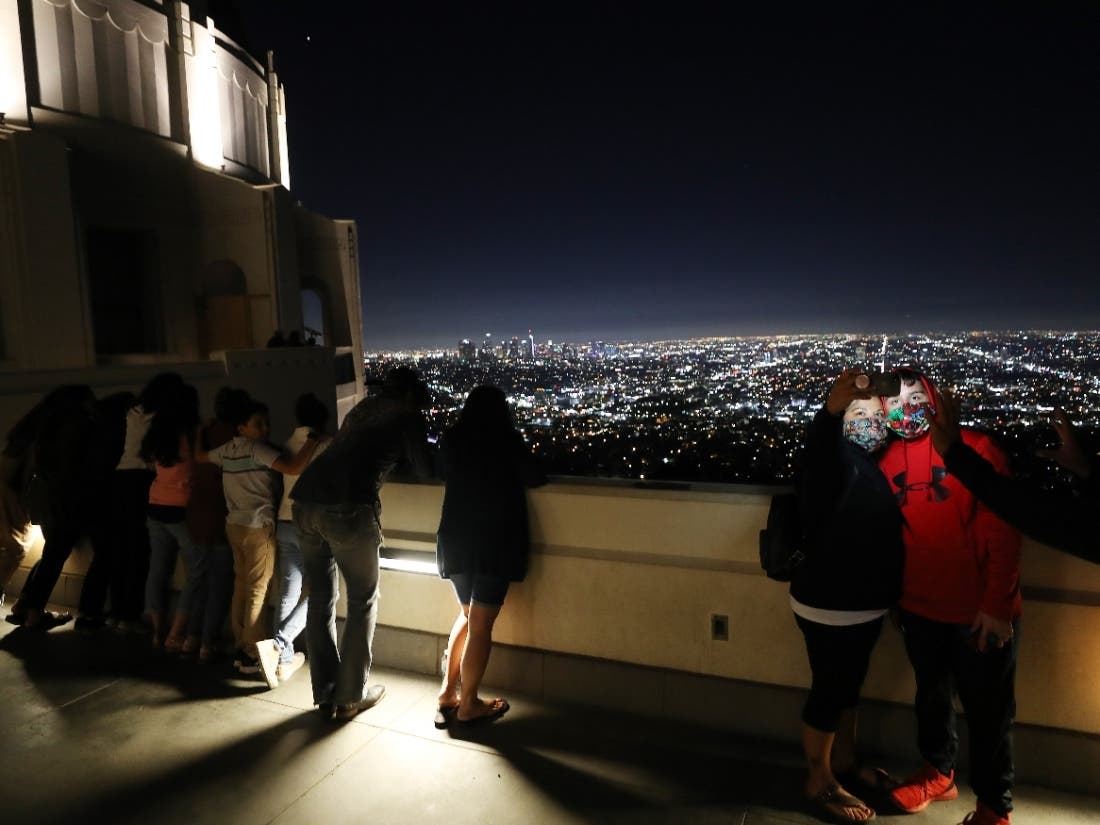 People pose for a photo while wearing face masks at Griffith Observatory with downtown in the background amid the COVID-19 pandemic on July 16, 2020 in Los Angeles, California.