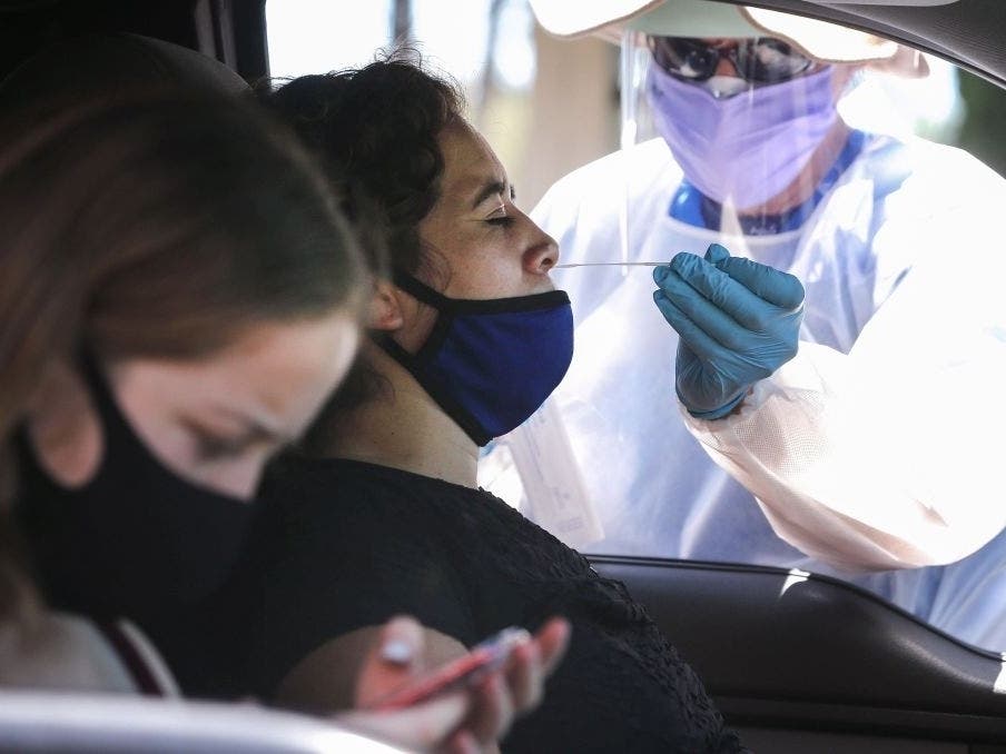 A healthcare worker assists a motorist with a nasal swab test at a drive-in coronavirus testing center on August 11, 2020 in Los Angeles.