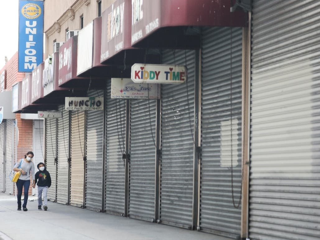 A woman and child wear face masks while walking past shuttered downtown clothing shops last month in the Los Angeles Fashion District.