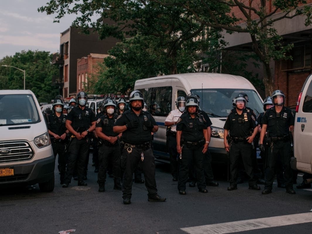 NYPD officers look on outside a police precinct building as protesters demand an end to systemic racism and police brutality during a march through Brooklyn on June 11.