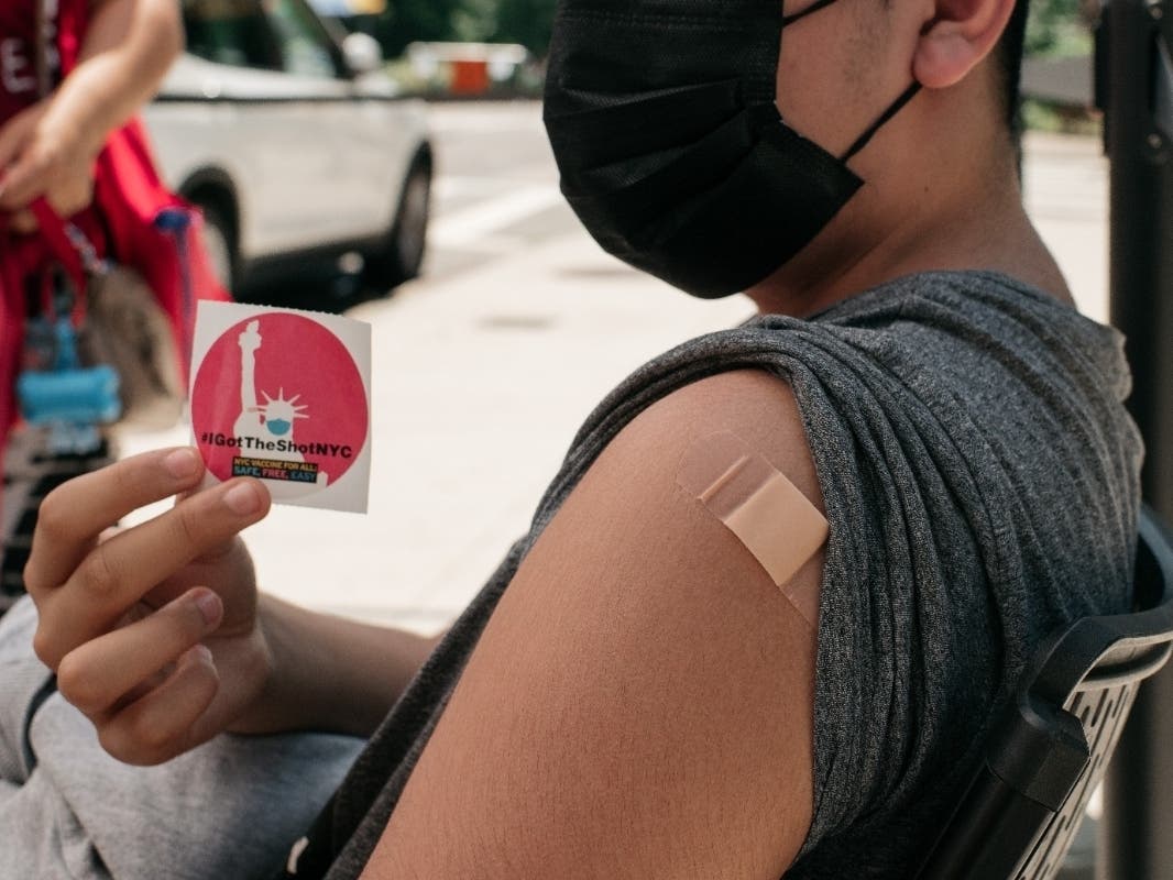 A 14-year-old newly vaccinated against COVID-19 holds up a sticker at a pop-up vaccination site on June 5 in Jackson Heights.