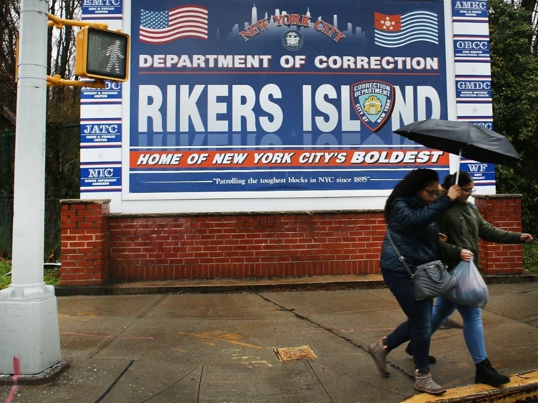 People walk by a sign at the entrance to Rikers Island on March 31, 2017.