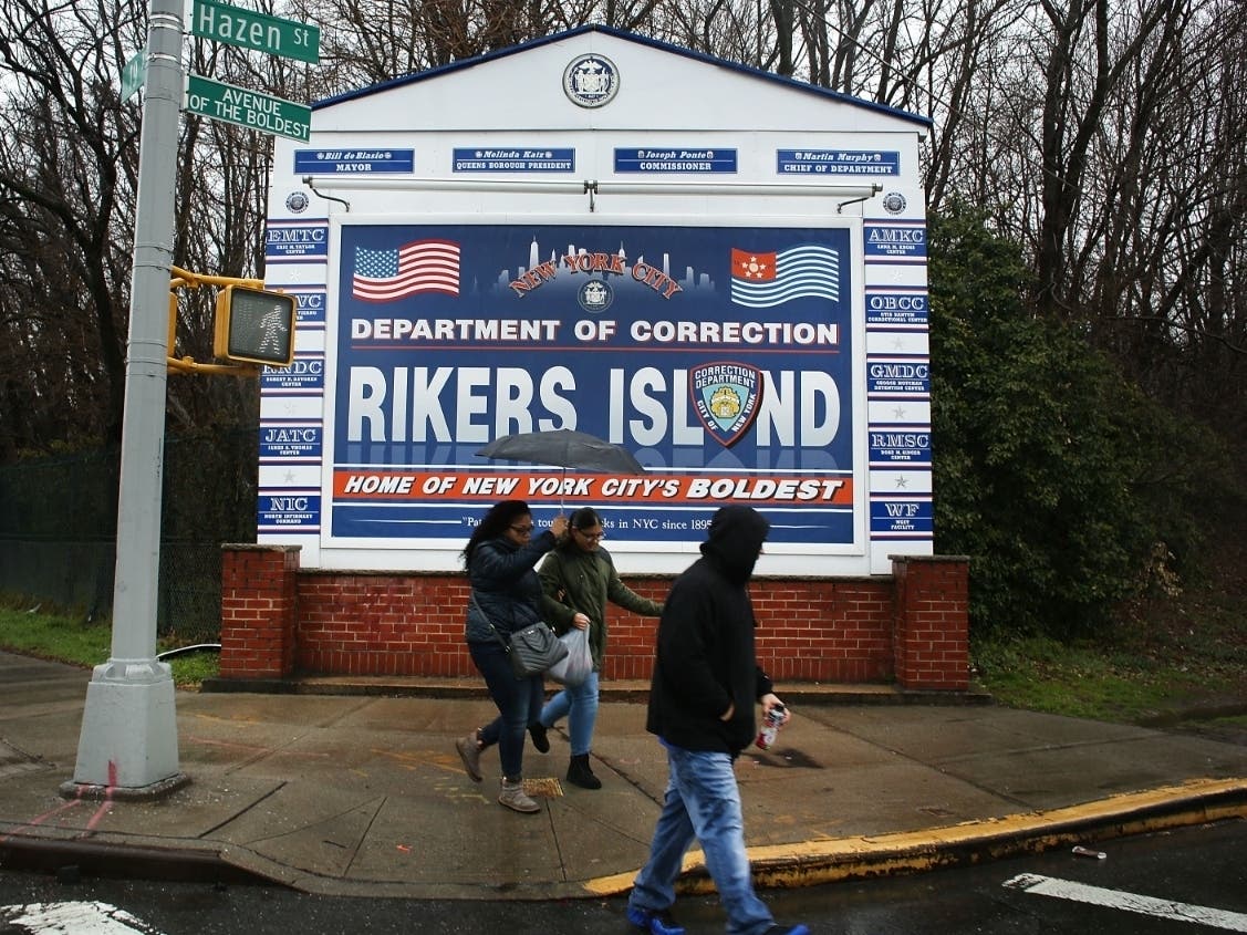  People walk by a sign at the entrance to Rikers Island on March 31, 2017.