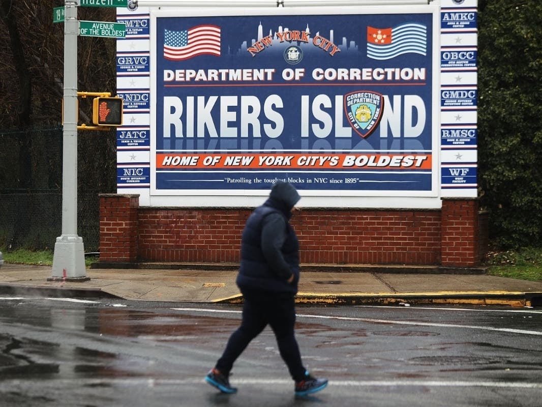 A woman walks by a sign at the entrance to Rikers Island on March 31, 2017.