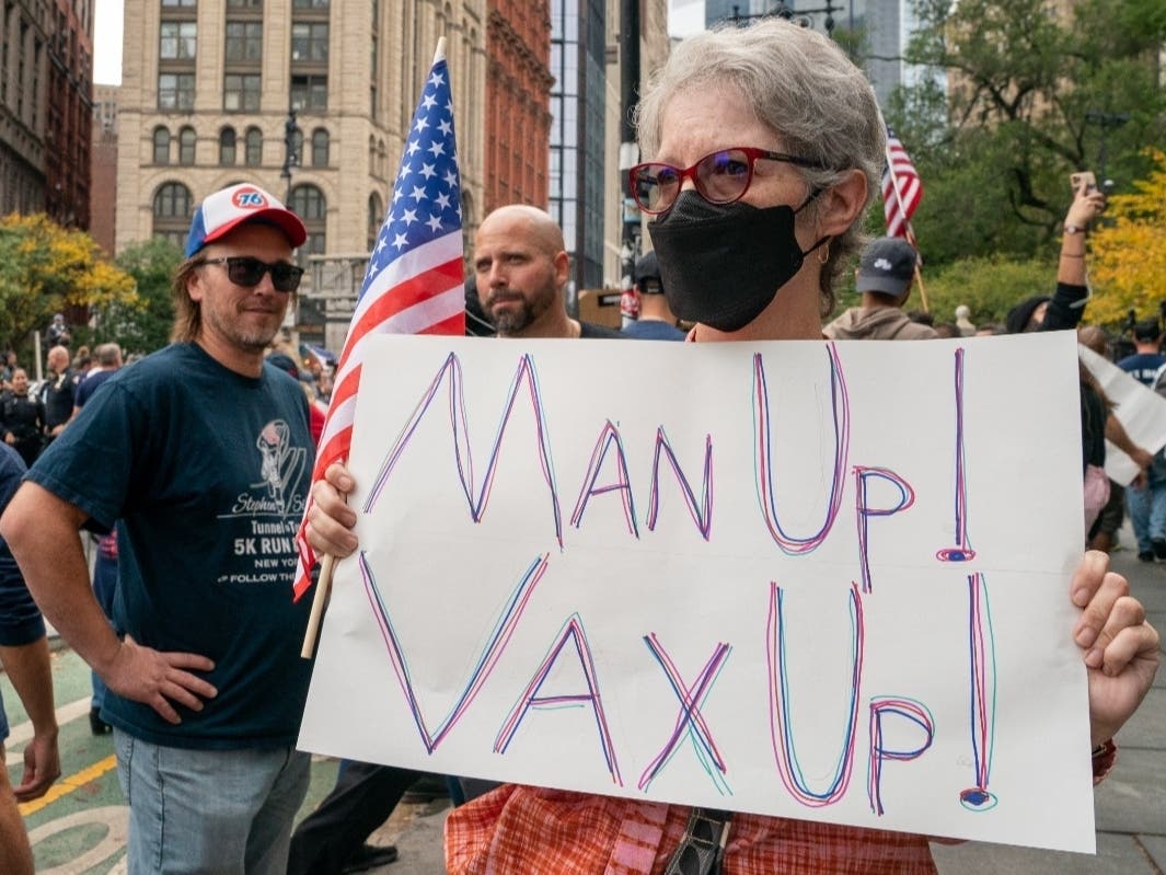 A person holds a sign urging people to get vaccinated at an anti-vax rally on Monday. All city workers, excluding uniformed correction officers, are required to have at least one dose of the COVID-19 vaccine by Friday at 5 p.m.