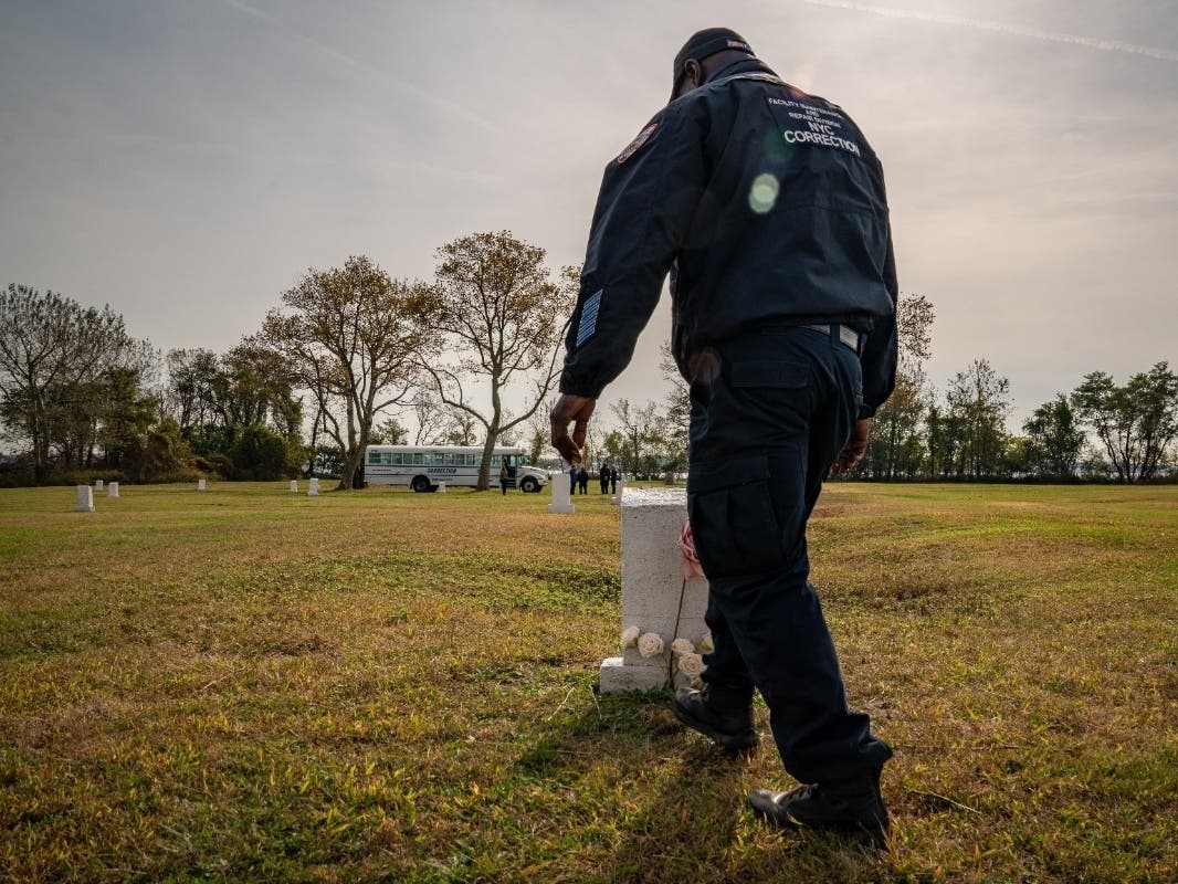 A Department of Correction officer walks by flowers laid at a burial marker on Hart Island, a former prison and Nike missile silo site which is now the largest public burial ground in the United States, on Oct. 25, 2019.