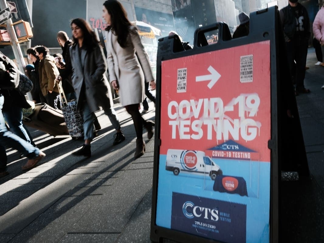 People walk by groups of people lined-up to get tested for Covid-19 in Times Square on Dec. 5.