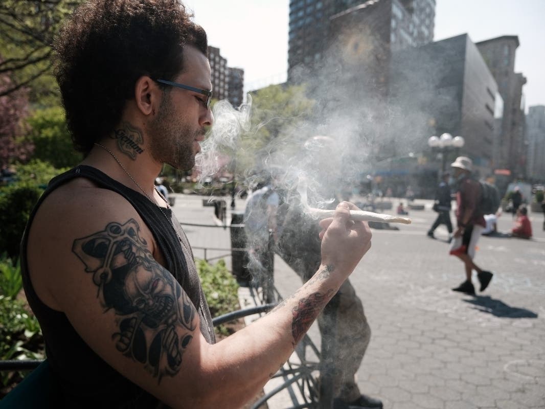A man smokes marijuana as people line up to receive a free marijuana cigarette after showing proof of a COVID-19 vaccination at Union Square on April 20, 2021.
