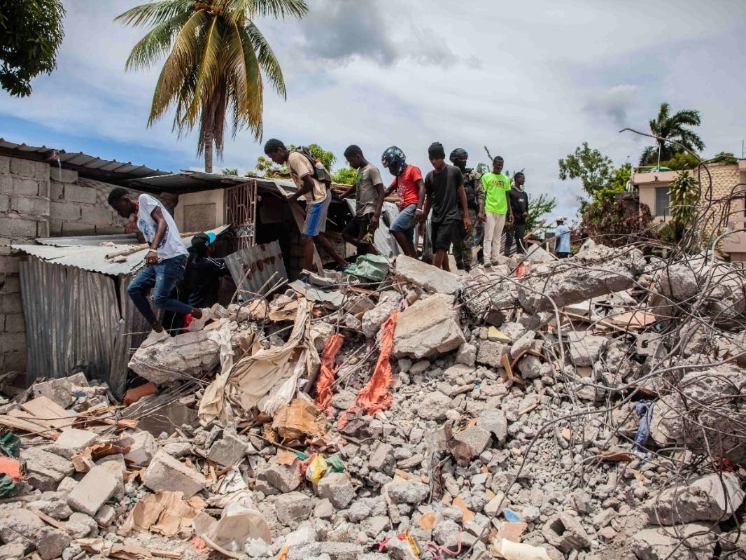 People walk over a pile of rubble from a collapsed building after a 7.2-magnitude earthquake struck Haiti on August 16, 2021 in Les Cayes, Haiti.