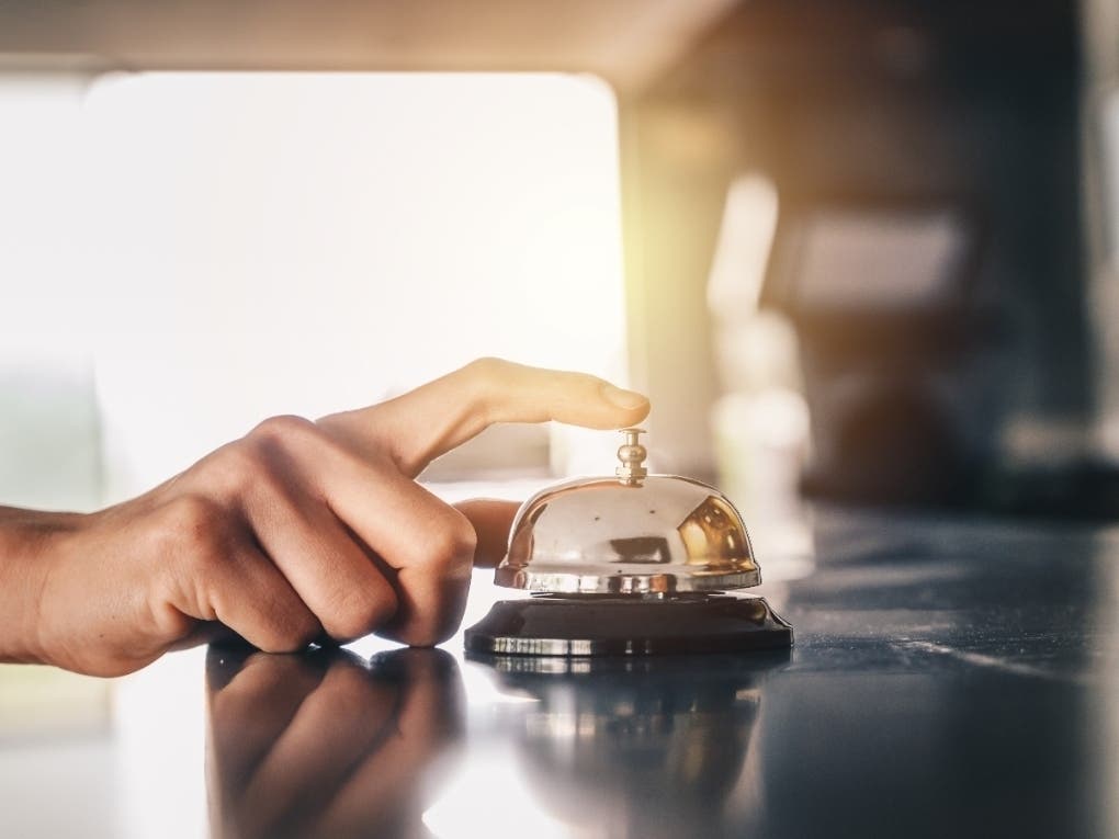Close-up of someone hand trying to call hotel reception by ringing front desk bell.