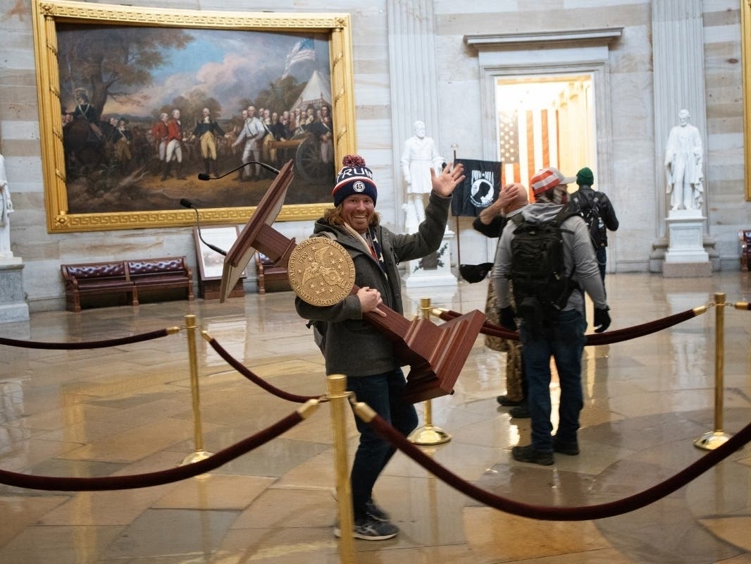 Adam Christian Johnson, 36, has been identified in a viral image of a man taking a U.S. House lectern. He was arrested on a federal warrant.