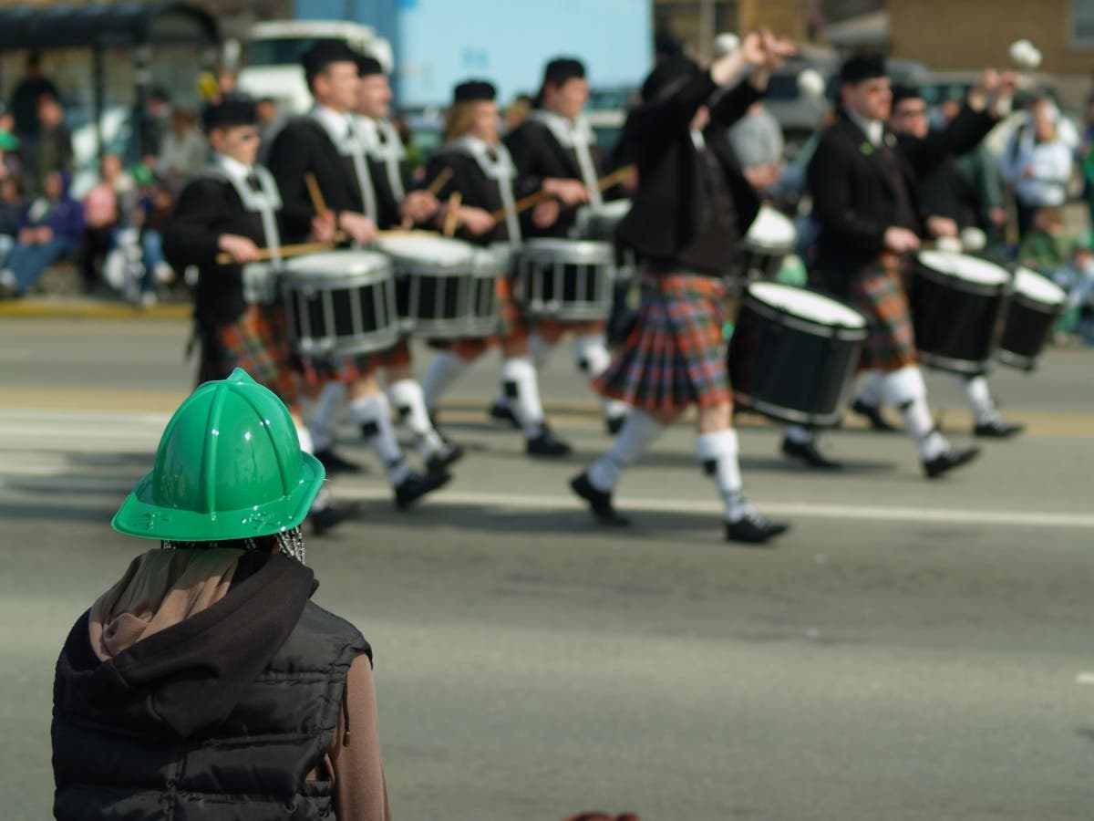 A file photo of a person in green hat watching drummers walk by in the St. Patrick’s Day parade.