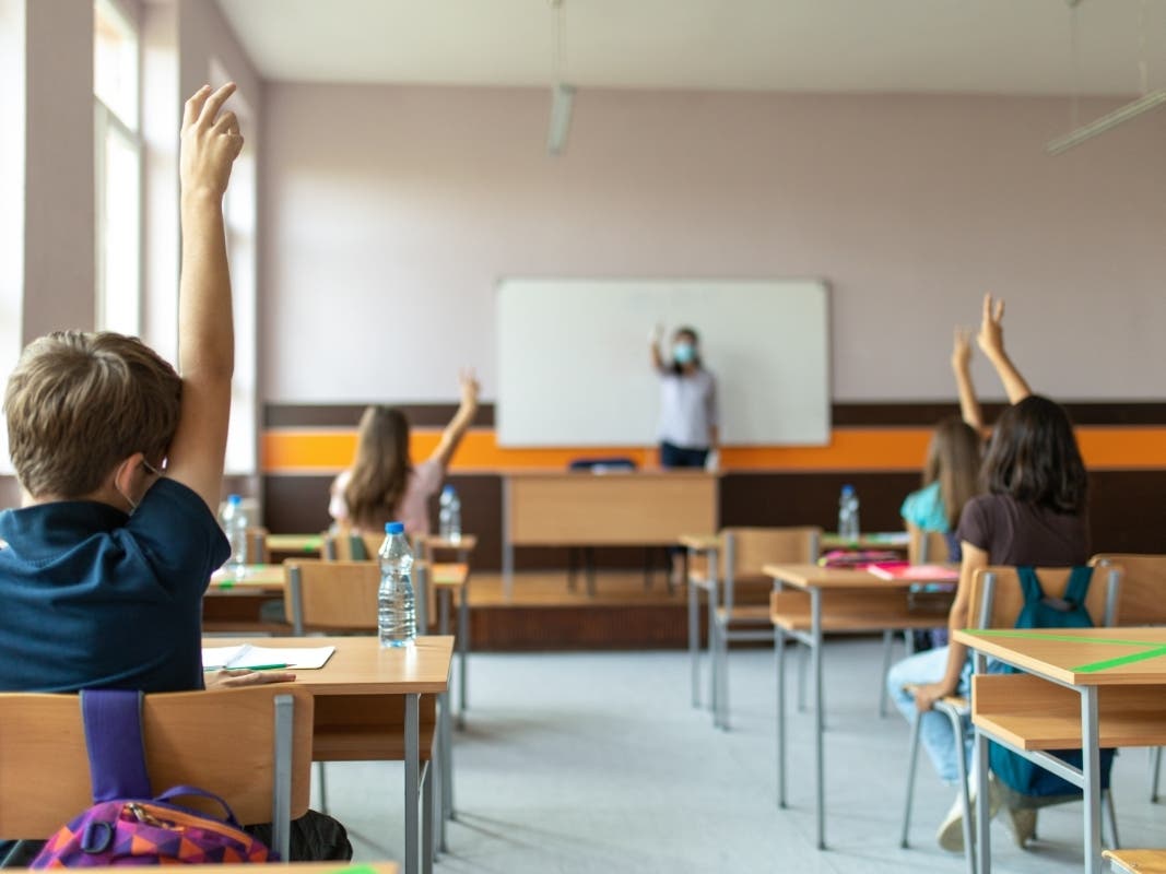 A file photo of atudents with protective masks sitting in school desks in their classroom. School desks are marked with a cross to mark a place where sitting is not allowed to maintain social distance during the coronavirus pandemic.