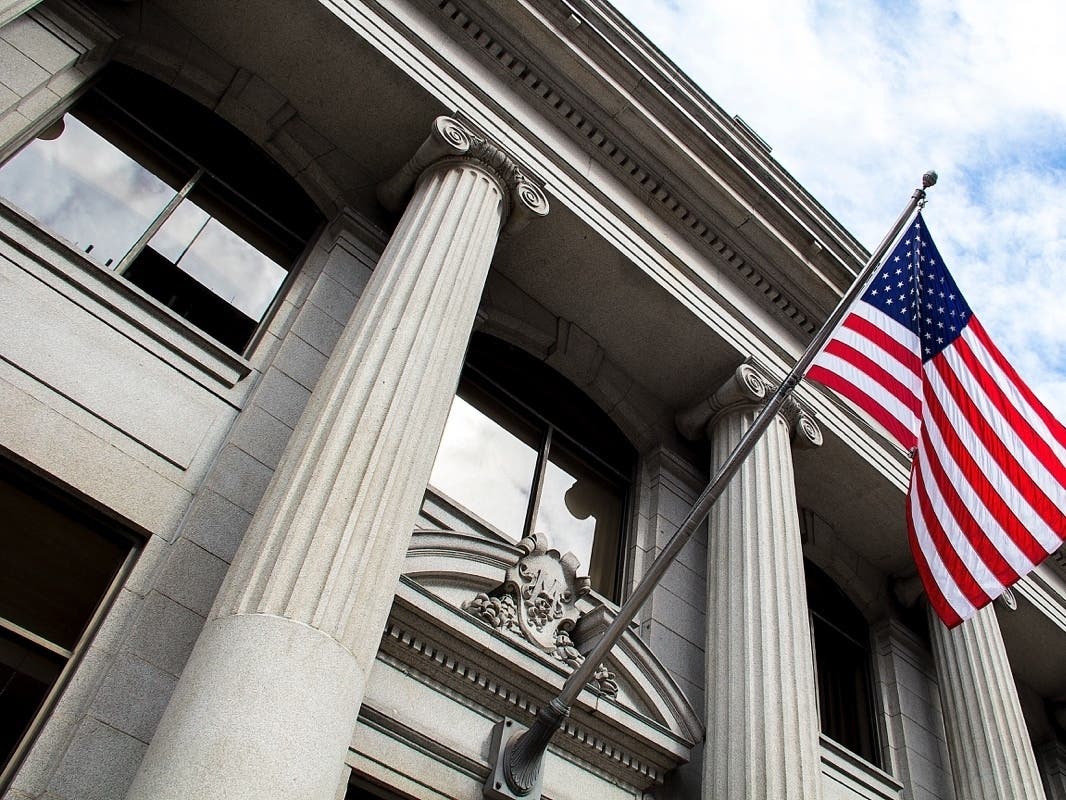 American flag flying over government building in city, blue sky and clouds