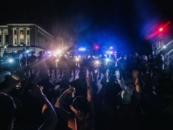 Demonstrators sit in the street in front of law enforcement on Tuesday Kenosha. As the city declared a state of emergency curfew, a third night of civil unrest occurred after the shooting of Jacob Blake, 29. 