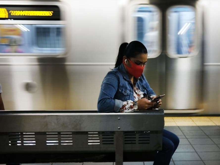 People, most with face masks, wait on a ride on a New York City subway platform.