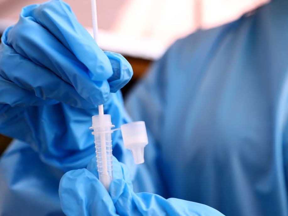 A registered nurse stirs a nasal swab in testing solution after administering a COVID-19 test at Sameday Testing in Los Angeles.